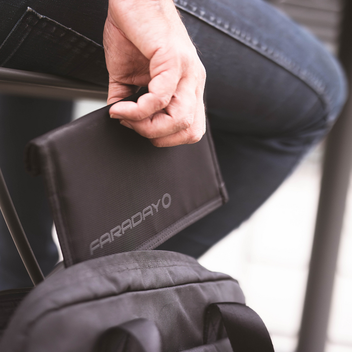 Faraday Jacket Pro Cordura phone bag held by a person sitting on a chair, showcasing sleek design and magnetic closure.