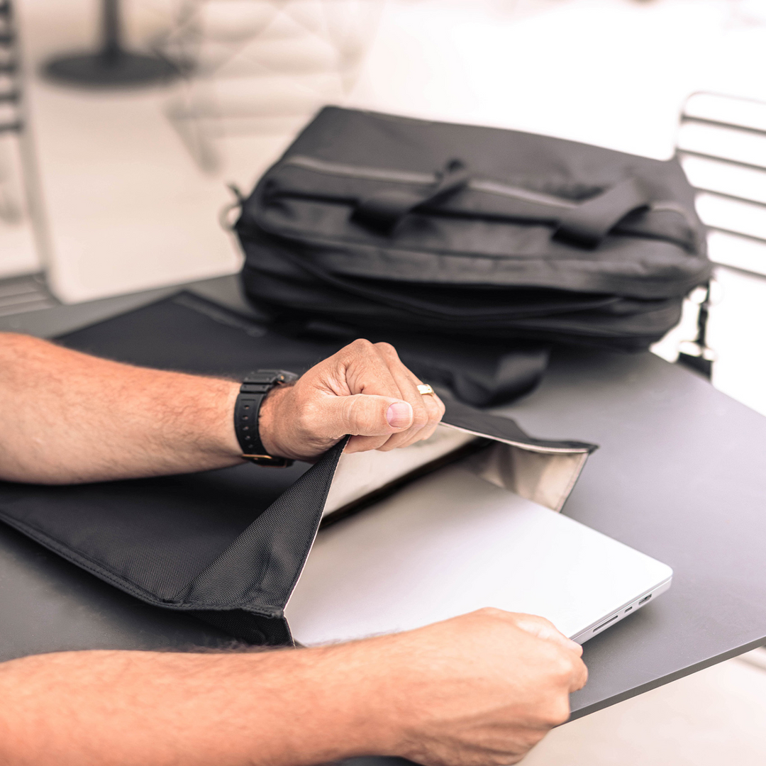 Person using the Faraday Jacket Pro Cordura laptop bag with magnetic closure on a table.