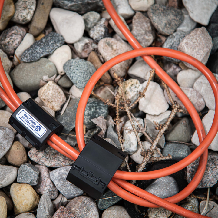 Faraday Broadband EMP Ferrite cables lying on rocky ground for high frequency noise suppression.