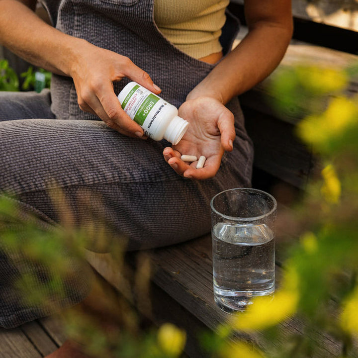 Real Mushrooms Ergo + L-Ergothioneine supplement being poured into a hand with a glass of water nearby.