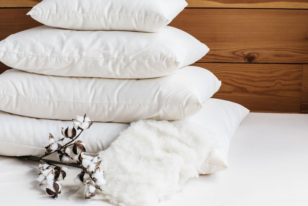 Holy Lamb Bed Pillows stacked on a surface with a cotton branch and wool, showcasing comfort and natural materials.