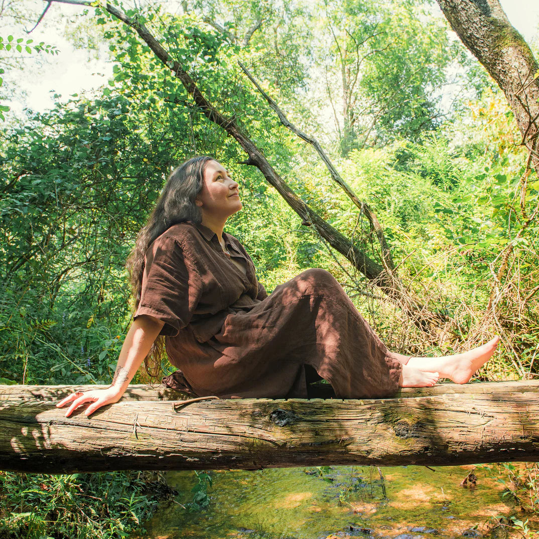 Woman enjoying nature on a log in a lush green forest, embodying relaxation and mindfulness.