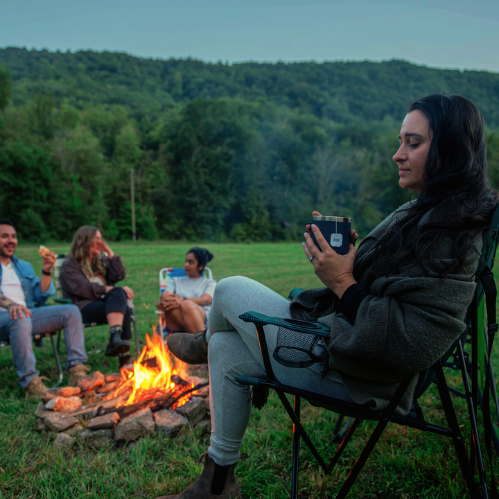 Group of friends relaxing around a campfire in the evening, enjoying snacks and drinks in nature.