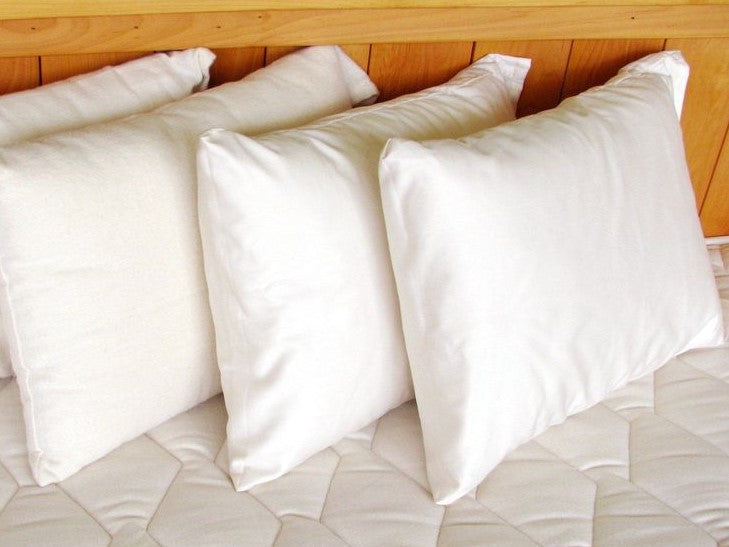 Holy Lamb Organics Travel Pillow displayed on a bed, featuring multiple white pillows for ultimate comfort.