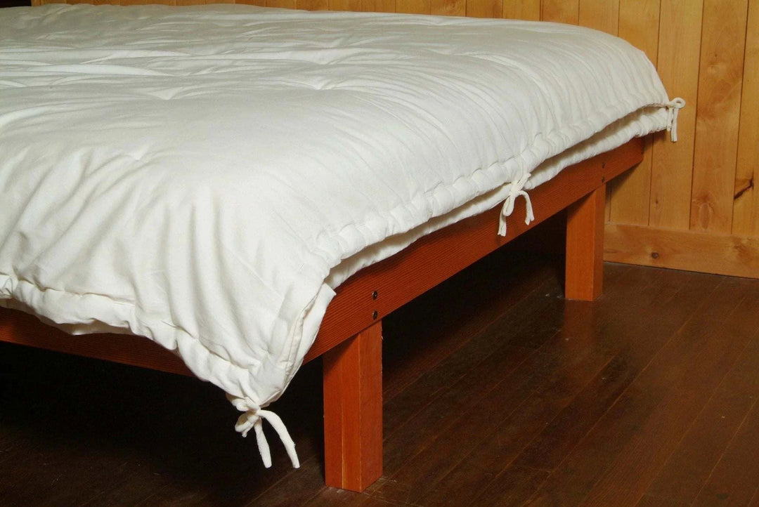 Holy Lamb Organics Comforter on a wooden bed frame with ties visible, showcasing its all-season design.