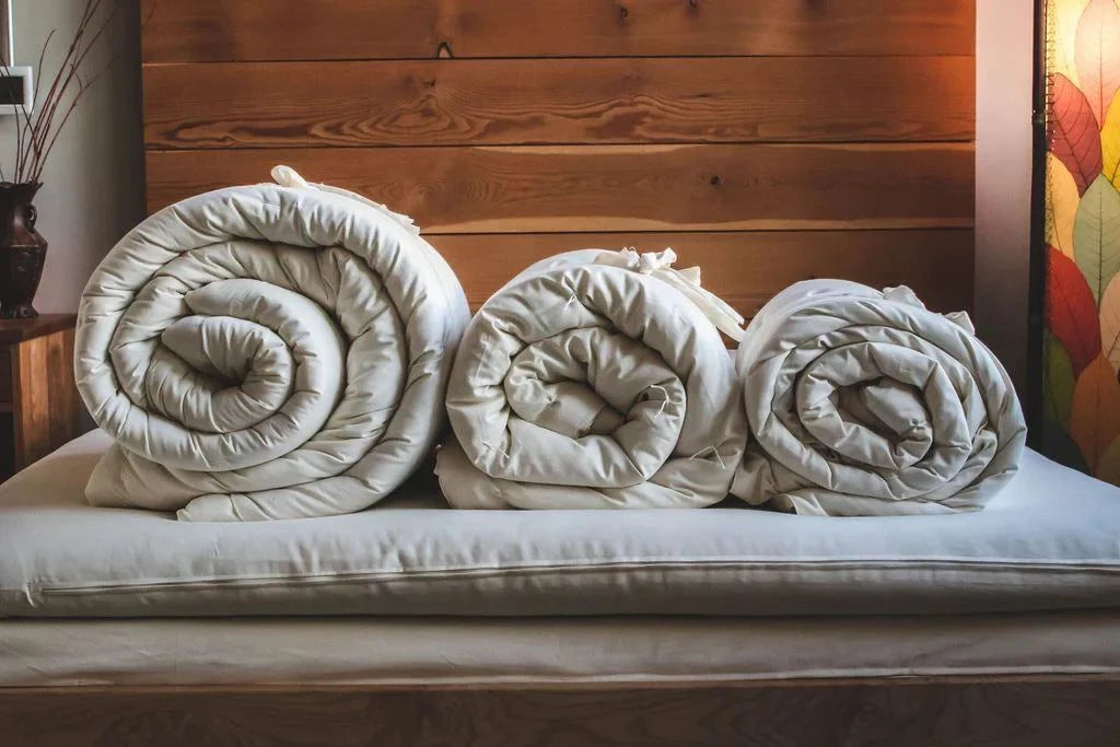 Holy Lamb Organics Comforter rolls displayed on a bed, showcasing premium organic wool comforters.