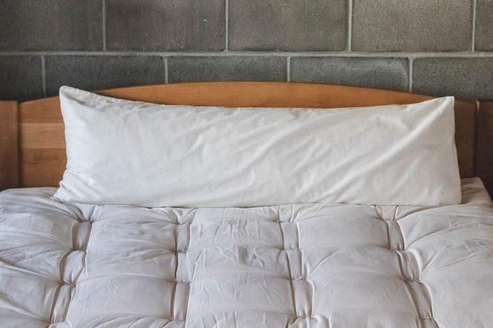 Holy Lamb Organics Body Pillow on a bed, showcasing its natural wool-filled and full-size design.