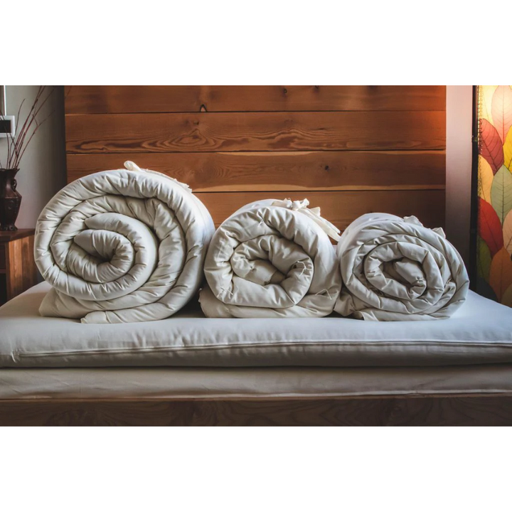 Holy Lamb Organics Comforter in three rolled sizes displayed elegantly on a bed, showcasing organic wool warmth.